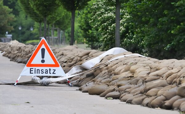Bild vergr&ouml;&szlig;ern: Warnschild mit Aufschrift "Einsatz" an Straße mit Sandsäcken und Entwässerungsschlauch